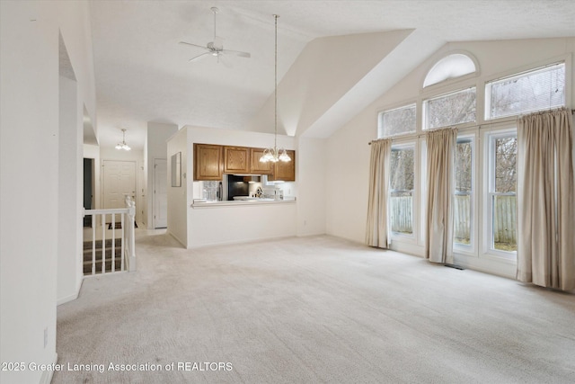 unfurnished living room with ceiling fan with notable chandelier, high vaulted ceiling, and light colored carpet