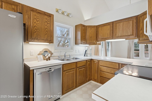 kitchen featuring stainless steel appliances, a sink, vaulted ceiling, light countertops, and brown cabinetry