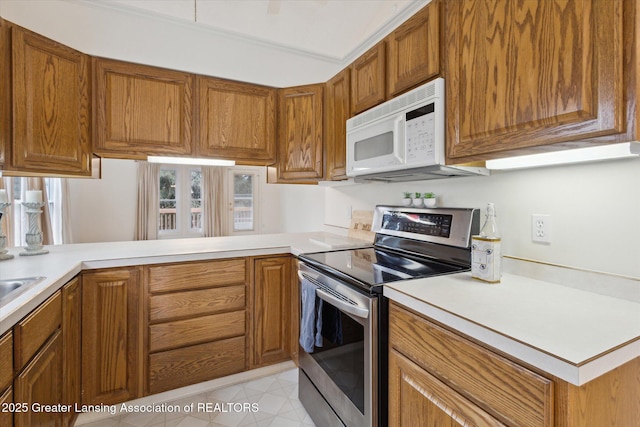 kitchen featuring brown cabinets, white microwave, stainless steel electric range oven, and light countertops