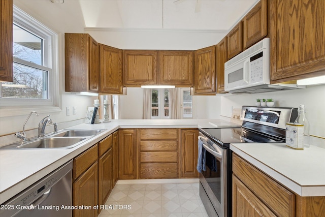 kitchen with a sink, light countertops, appliances with stainless steel finishes, brown cabinets, and light floors