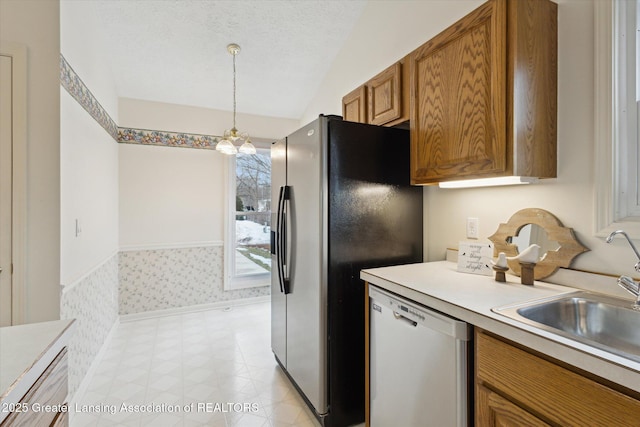 kitchen with a textured ceiling, light countertops, hanging light fixtures, dishwasher, and brown cabinetry