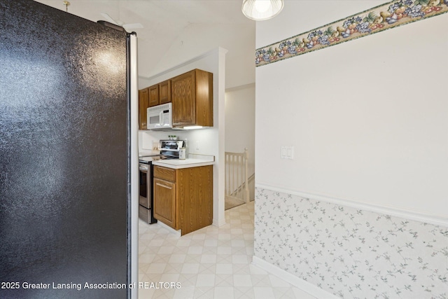 kitchen featuring lofted ceiling, white microwave, light countertops, light floors, and stainless steel range with electric stovetop