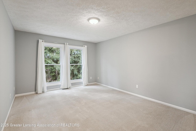 spare room with light colored carpet, a textured ceiling, and baseboards