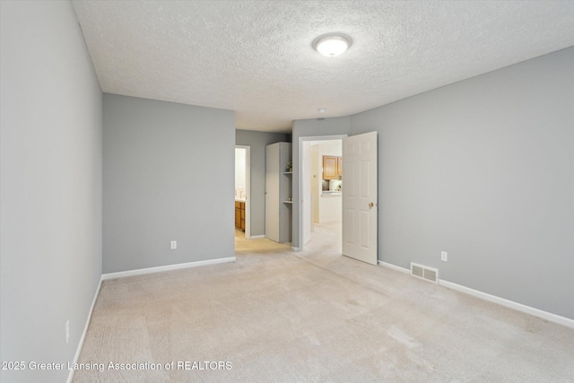 unfurnished bedroom with light carpet, visible vents, baseboards, a spacious closet, and a textured ceiling