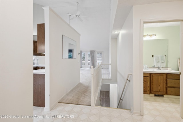 hall featuring light colored carpet, a sink, an upstairs landing, baseboards, and light floors