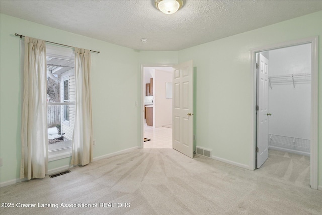 unfurnished bedroom featuring visible vents, a textured ceiling, and light colored carpet