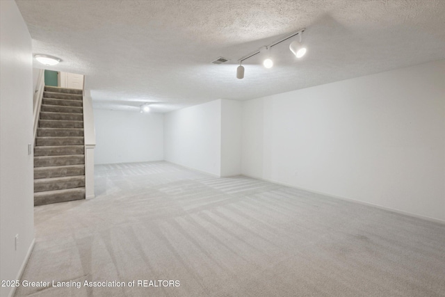 finished basement featuring visible vents, light colored carpet, stairway, and a textured ceiling