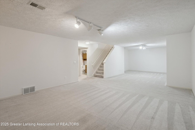 finished basement featuring stairs, a textured ceiling, visible vents, and light colored carpet