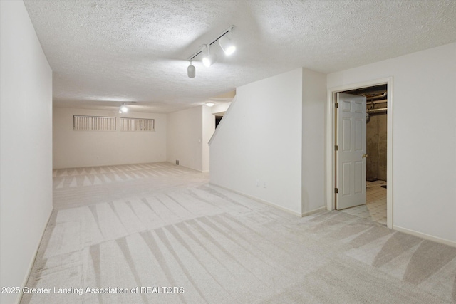 finished below grade area with light carpet, a textured ceiling, rail lighting, and baseboards