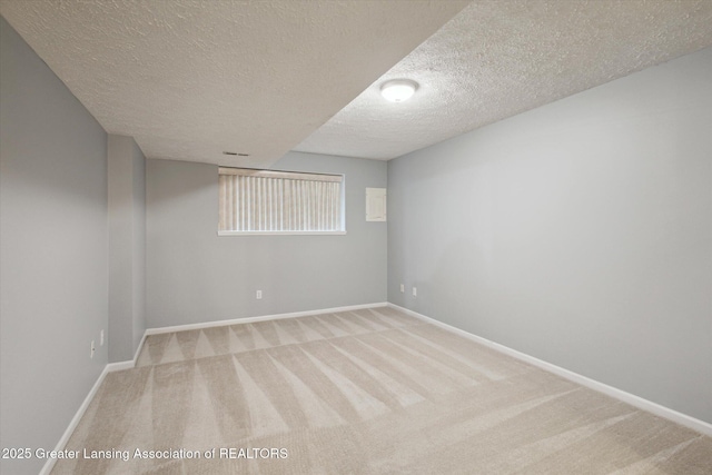 empty room with light carpet, a textured ceiling, and baseboards