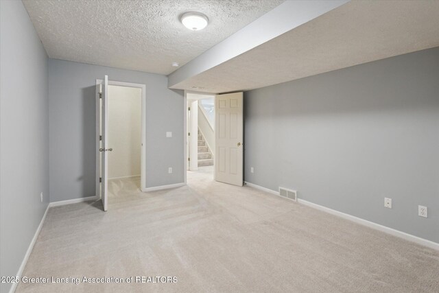 finished basement featuring light colored carpet, visible vents, stairway, a textured ceiling, and baseboards