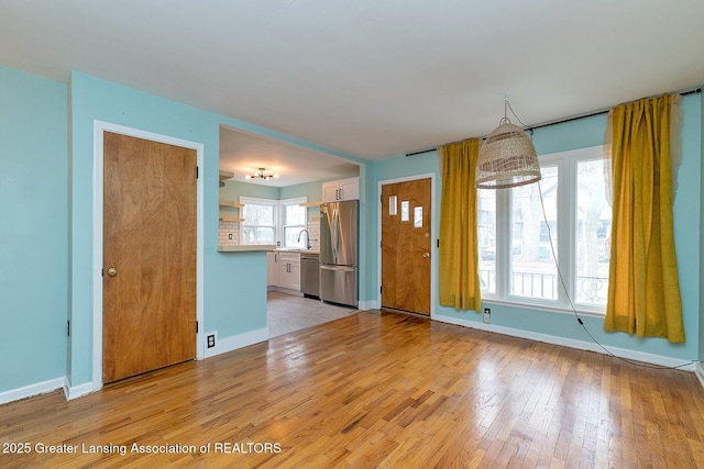 unfurnished living room featuring light wood finished floors, a sink, and baseboards