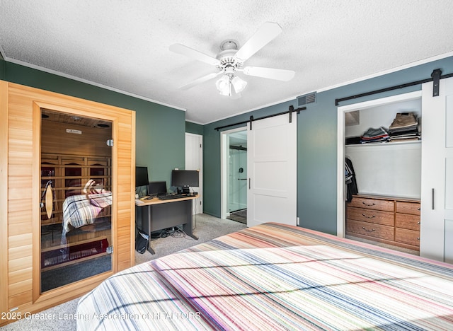 carpeted bedroom with visible vents, crown molding, a textured ceiling, and a barn door