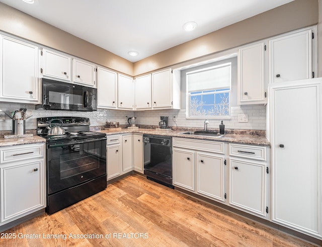 kitchen with light wood-style flooring, a sink, white cabinets, black appliances, and tasteful backsplash