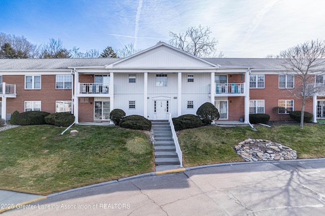 view of front of property featuring a front yard, a balcony, and brick siding