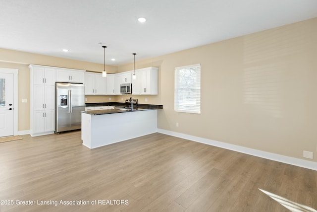 kitchen with stainless steel appliances, a peninsula, a sink, white cabinetry, and dark countertops