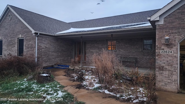 exterior space with a shingled roof and brick siding