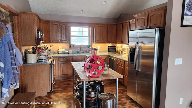 kitchen with dark wood-style flooring, stainless steel appliances, a textured ceiling, light countertops, and a sink