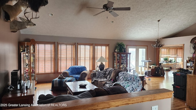 living room featuring ceiling fan with notable chandelier, vaulted ceiling, a textured ceiling, and wood finished floors