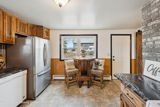 kitchen with a wainscoted wall, brown cabinetry, wooden walls, dark stone counters, and dishwasher