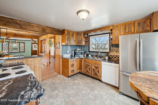 kitchen with stainless steel appliances, brown cabinetry, a sink, and dark stone countertops