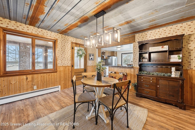 dining area with light wood finished floors, wainscoting, wooden ceiling, baseboard heating, and wood walls