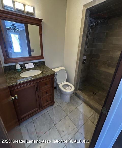 bathroom featuring toilet, a ceiling fan, vanity, tiled shower, and tile patterned floors