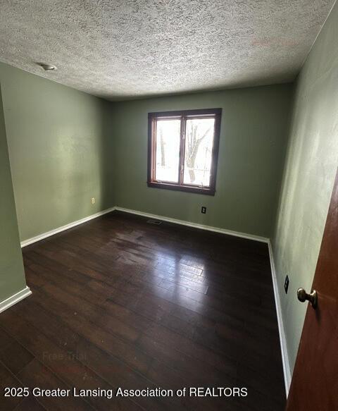 empty room featuring a textured ceiling, dark wood-type flooring, and baseboards