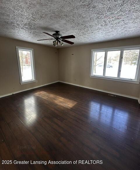 empty room featuring a textured ceiling, ceiling fan, dark wood-style flooring, and baseboards