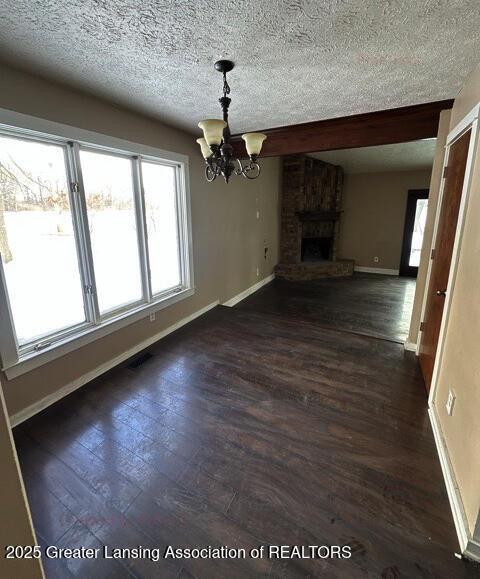 unfurnished living room featuring baseboards, dark wood-style flooring, a textured ceiling, a fireplace, and a notable chandelier