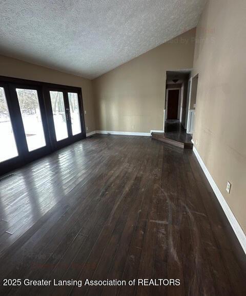 unfurnished living room with dark wood-type flooring, vaulted ceiling, a textured ceiling, and baseboards