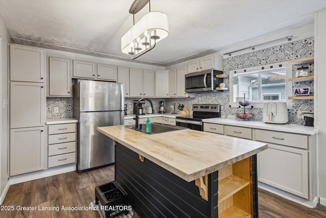 kitchen featuring dark wood finished floors, appliances with stainless steel finishes, a sink, open shelves, and wooden counters