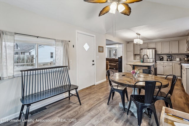 dining space with light wood finished floors, visible vents, baseboards, a ceiling fan, and vaulted ceiling