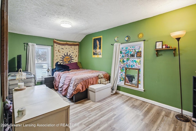 bedroom with vaulted ceiling, a textured ceiling, baseboards, and wood finished floors