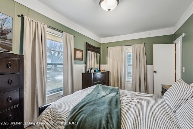 bedroom featuring multiple windows, ornamental molding, and wainscoting