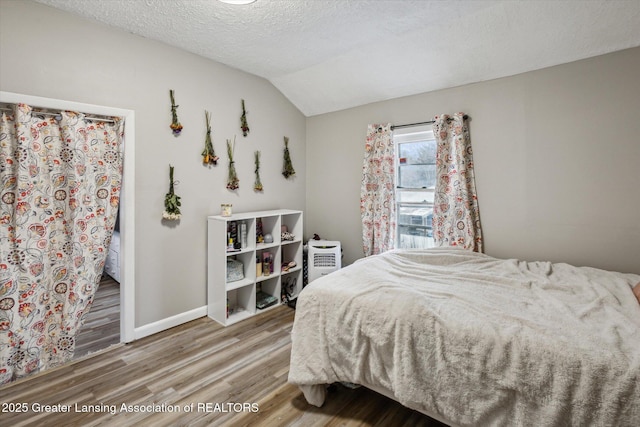 bedroom featuring vaulted ceiling, a textured ceiling, baseboards, and wood finished floors