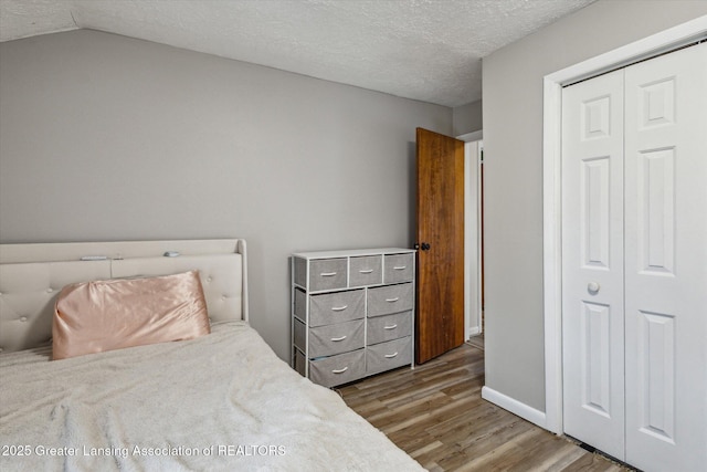 bedroom featuring a textured ceiling, lofted ceiling, wood finished floors, baseboards, and a closet