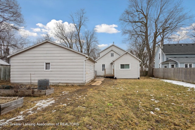 rear view of property featuring a lawn, fence, and a vegetable garden