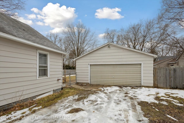 snow covered garage featuring a detached garage and fence