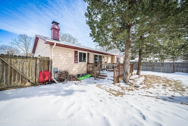 snow covered house with a chimney, fence, and a deck