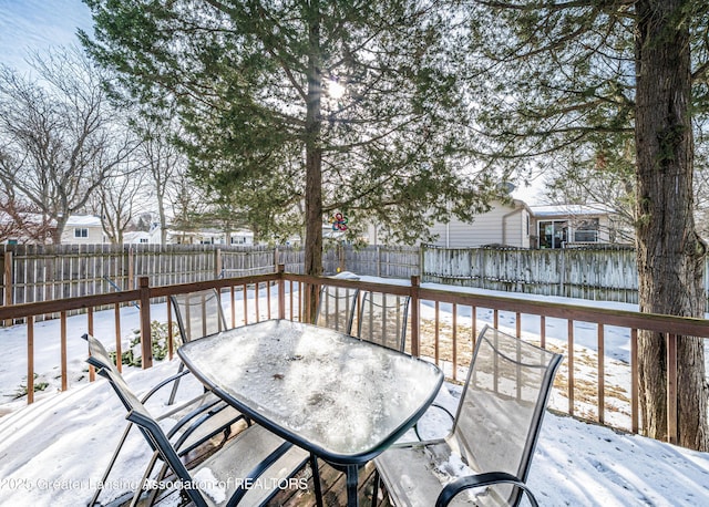 snow covered deck with outdoor dining space and a fenced backyard