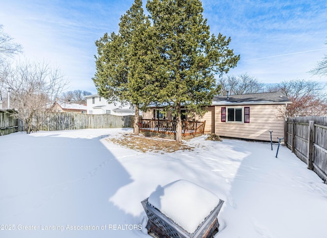 snow covered rear of property featuring a fenced backyard and a deck