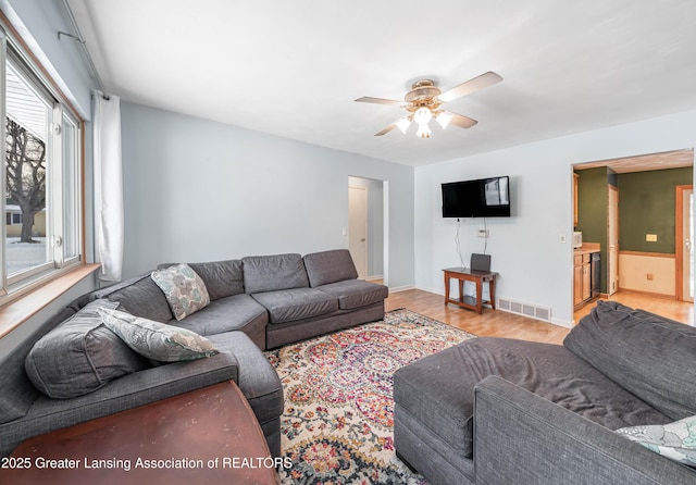 living room featuring light wood-style floors, visible vents, baseboards, and a ceiling fan