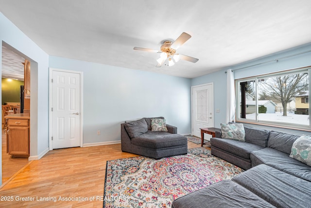 living room featuring a ceiling fan, baseboards, and light wood finished floors