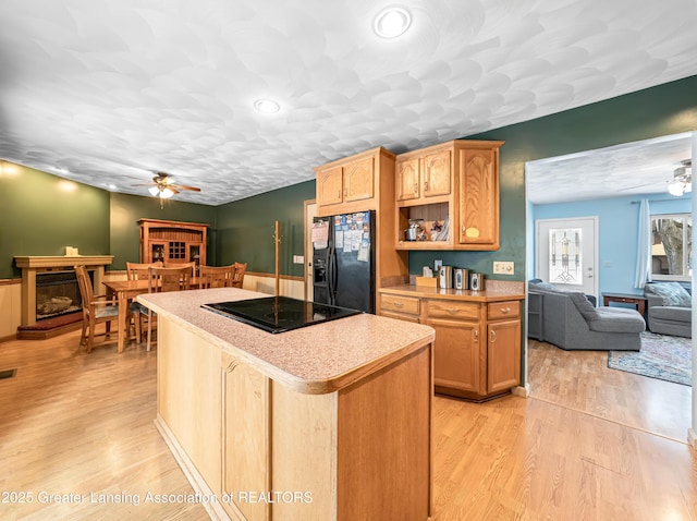 kitchen featuring black appliances, light wood-style flooring, a ceiling fan, and a center island