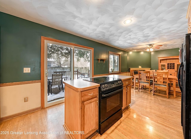 kitchen featuring light wood finished floors, a ceiling fan, a kitchen island, light countertops, and black appliances