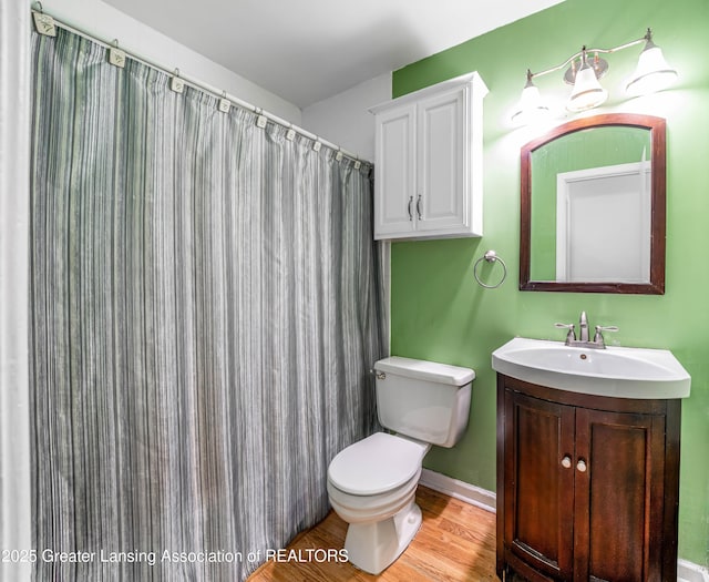 bathroom with toilet, a shower with shower curtain, wood finished floors, vanity, and baseboards