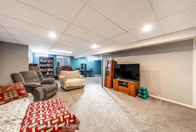 carpeted living area with a drop ceiling and baseboards