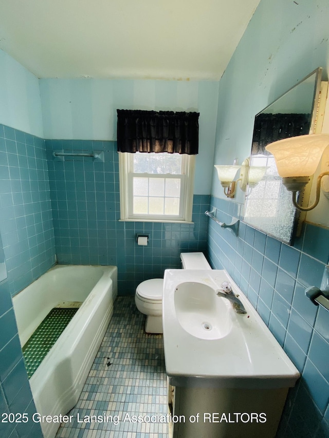 bathroom featuring tile patterned flooring, toilet, a bathing tub, a sink, and tile walls