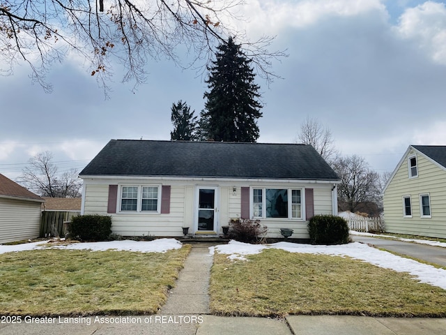 view of front of house featuring a shingled roof, fence, and a front lawn